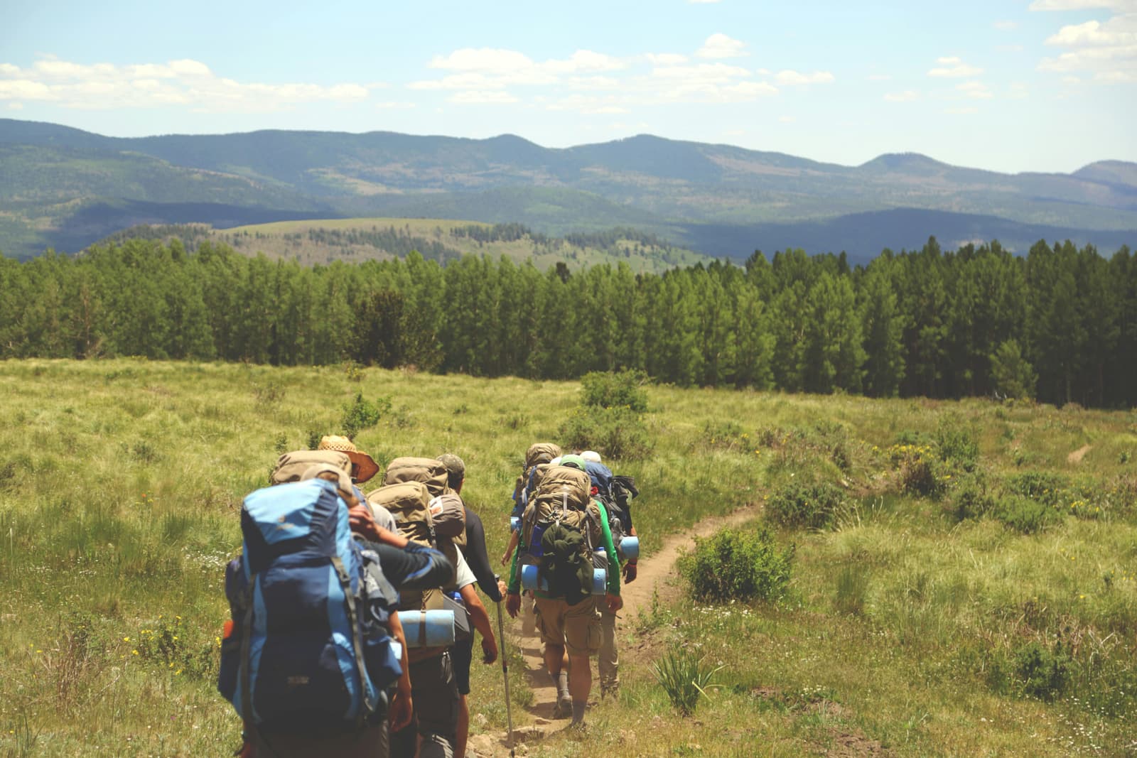 Hikers walking along a mountain trail with green hills ahead